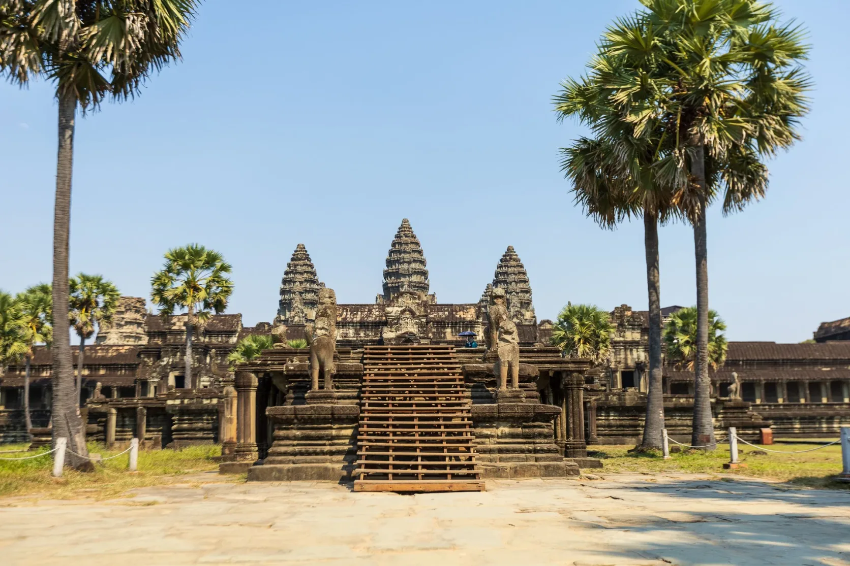 Angkor Wat's stone towers and entrance between palm trees.