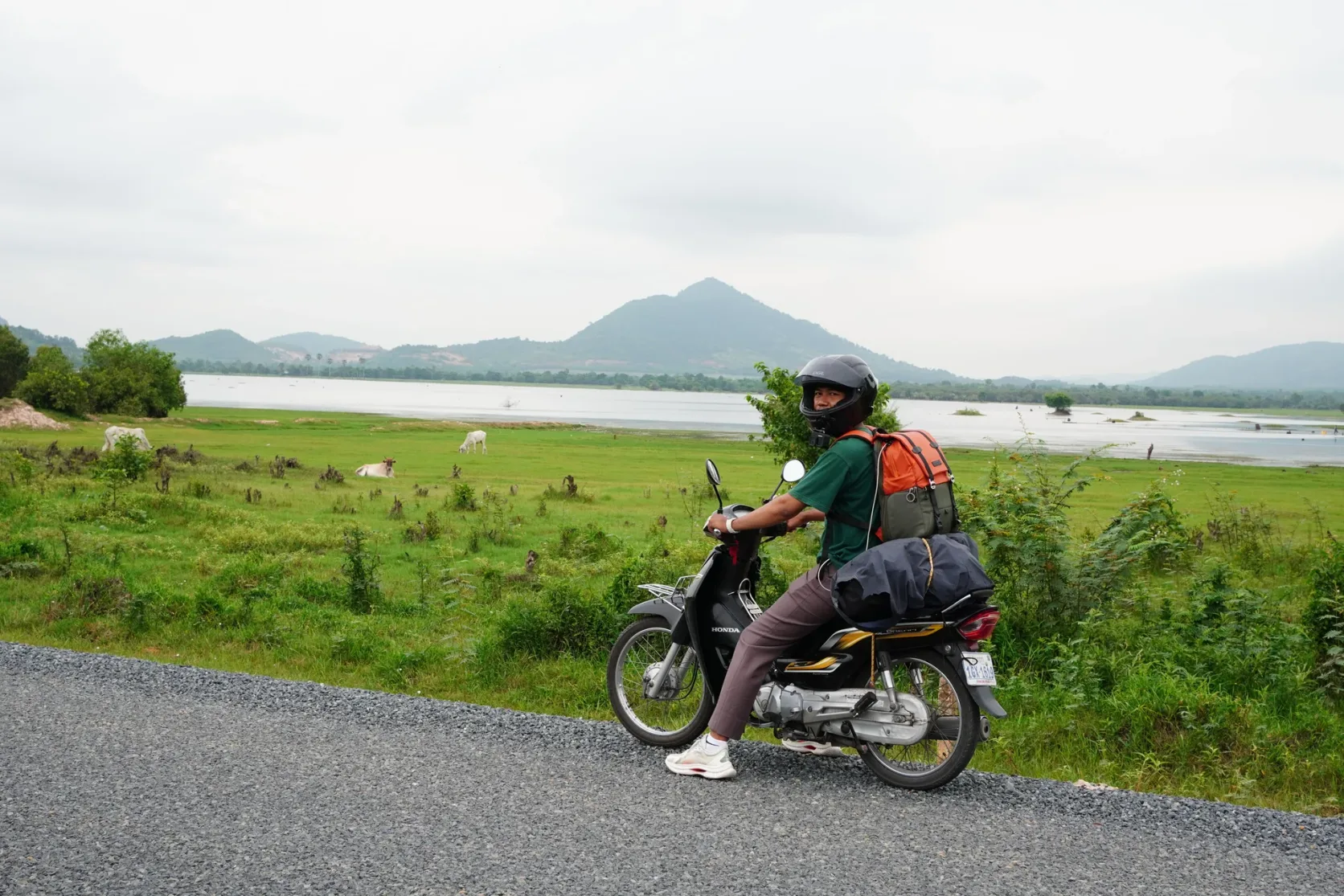 A motorcyclist beside green fields and hills near Kampot.