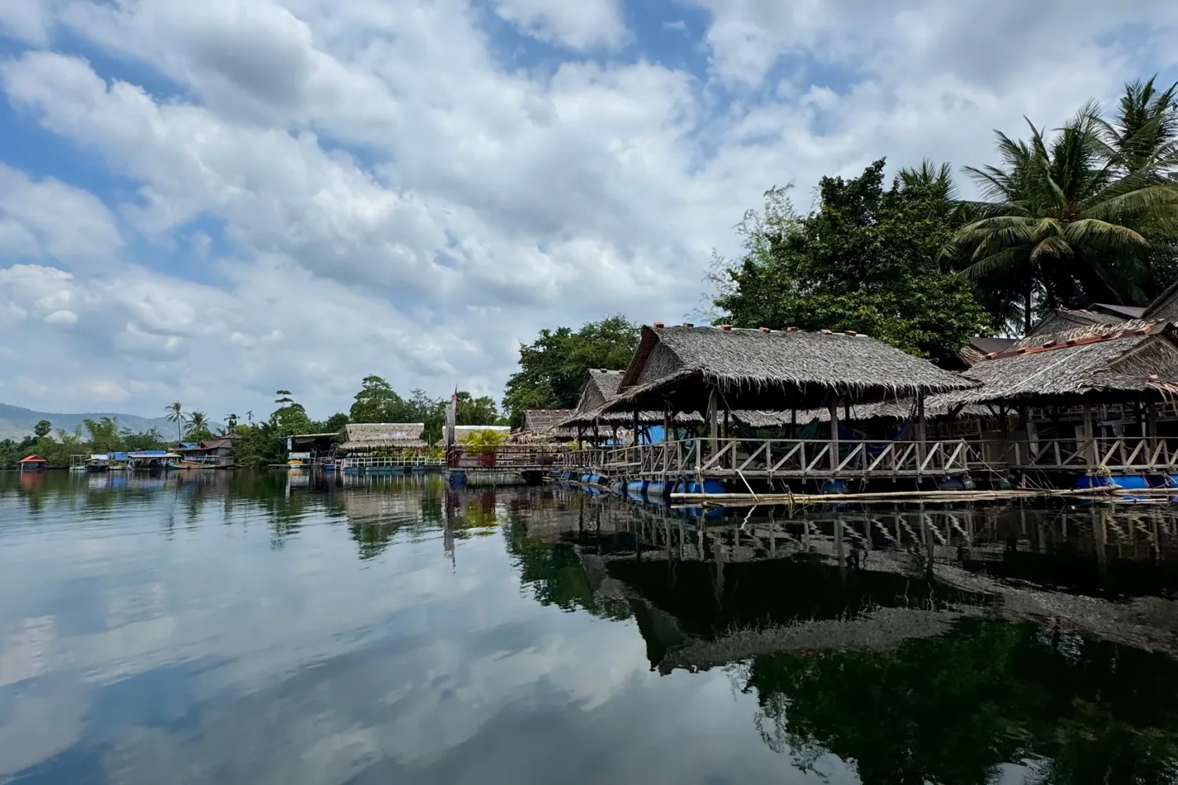 Wooden riverside huts reflected in calm water in Kampot.