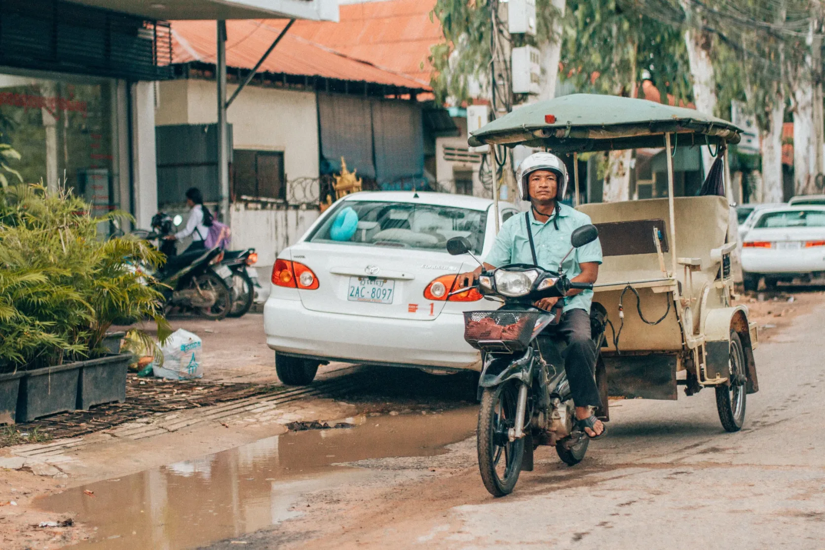 A driver riding a motorcycle tuk-tuk on a Siem Reap street.