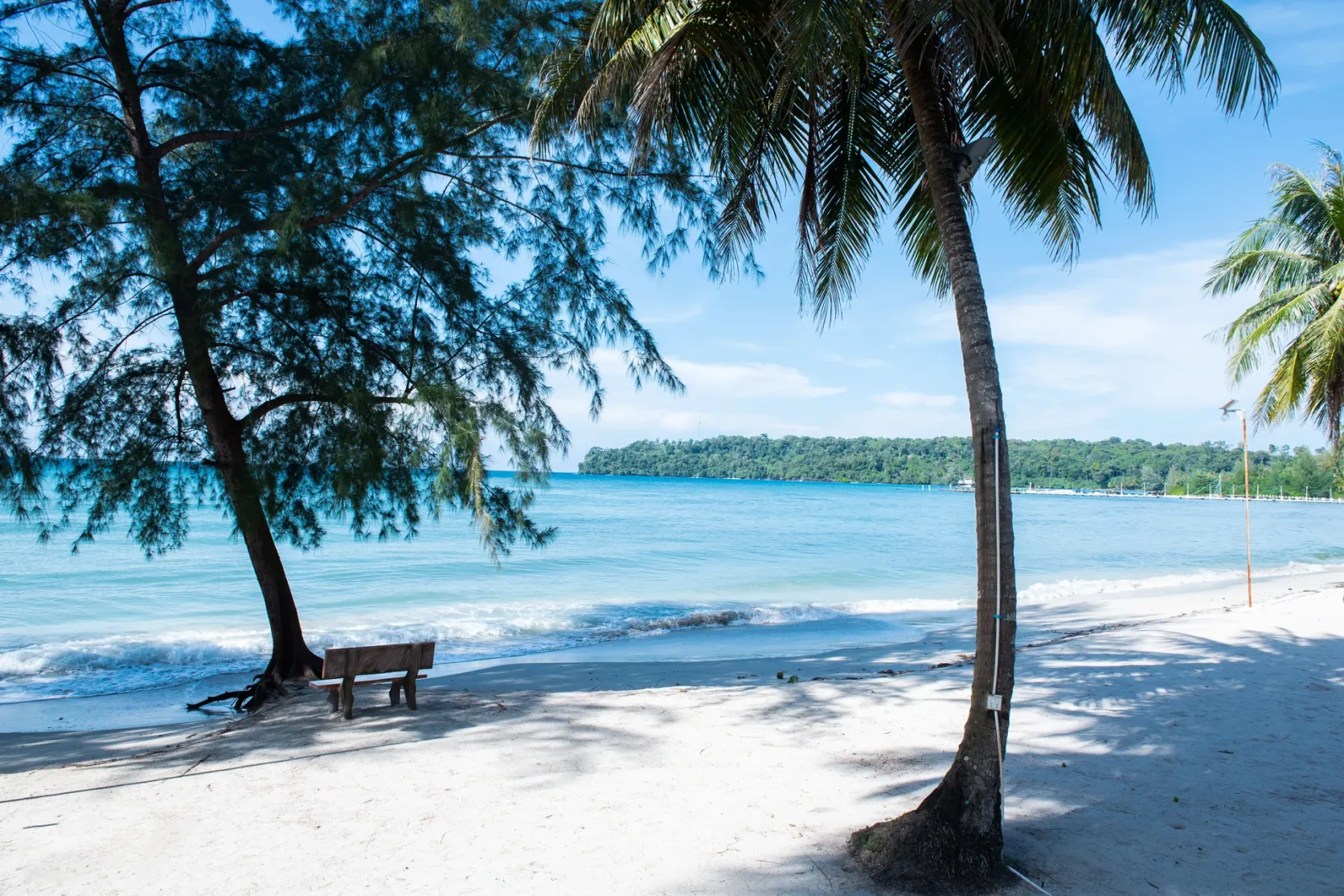 Tree shade on pale sand beside blue sea in Sihanoukville.