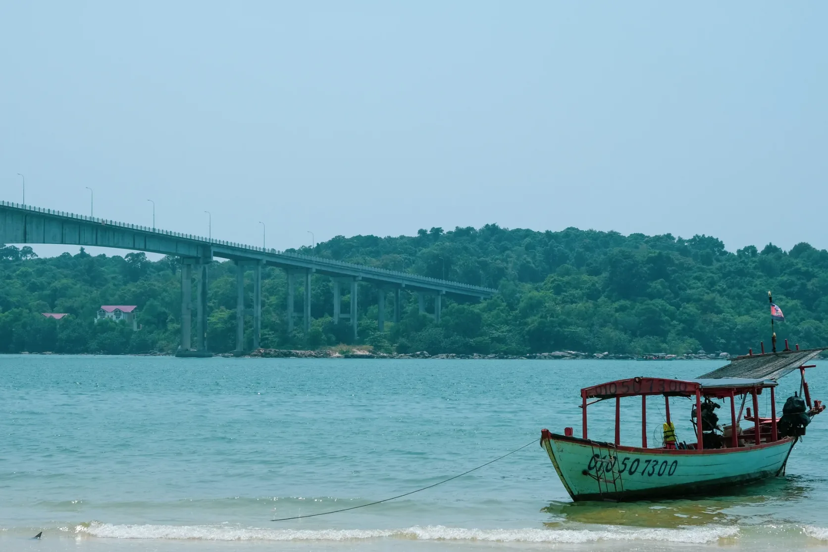 A wooden boat by the shore with a bridge in the distance.
